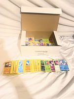 Open white cardboard box marked TERRATINTA containing large quantity of Pokémon cards with a row of cards laid out in front