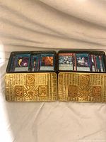 Both open gold tins filled with Yu-Gi-Oh! cards
