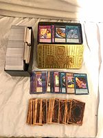 Gold embossed Yu-Gi-Oh! tin open with cards inside, stacks of cards in cardboard box and spread on table