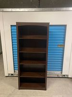 Front view of tall dark wood bookcase showing five shelves and curved top