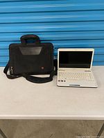Laptop and carrying bag on table, lid open showing white keyboard and screen