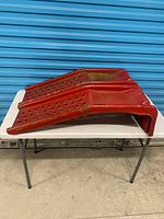 Pair of red stamped steel automotive ramps on table