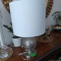 Full view of silver metal lamp with white drum shade on tabletop