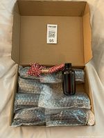 Open box showing bubble-wrapped bottles, rope, one unwrapped amber bottle