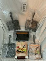 Group shot of four square cast iron mini skillets wrapped in bubble wrap, cast iron grill press, and small booklet
