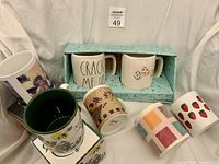 Group shot showing all seven mugs including boxed Rae Dunn set, Cherubin mug on its box, Friends Are Forever mug, multicolour, strawberry and pear tree mugs