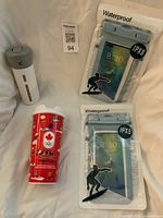 Group shot showing two packaged waterproof phone pouches, white/grey toiletry dispenser, and red Tim Hortons 2026 Olympic travel cup