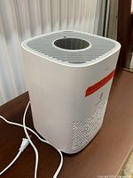 Left-side perspective of air purifier showing top circular grill and cord