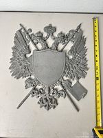 Front view of cast metal double-headed eagle plaque with measuring tape showing height