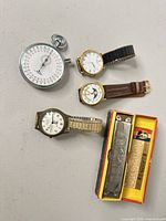 Group shot showing three wristwatches, stopwatch and harmonica with box