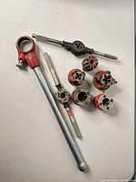 Overall view of pipe threader handle, six die heads and two T-handle die stocks