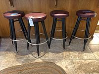 Four burgundy-seat swivel barstools with black metal legs and chrome footrests