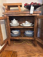 Overall view of cabinet with dishes, stool on top, fruit bowl