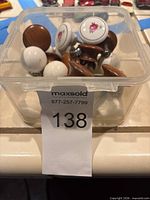 Clear bin containing mixed ceramic and wood cabinet knobs