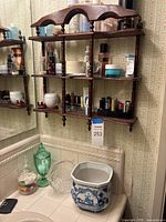 Overall view of wooden rack mounted on wall above countertop holding toiletries; decorative containers on counter include green glass lidded jar, clear glass dishes, ceramic planter