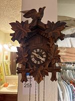 Front view of carved wooden cuckoo clock with bird, leaves, dial, hanging chains and weights visible