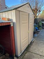Full front and side view of beige Rubbermaid shed beside red wooden structure