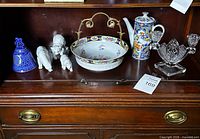 Shelf view showing bowl, coffee pot, bell, figurines, glass candle holder