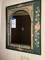 Front view of painted floral framed mirror mounted on wall