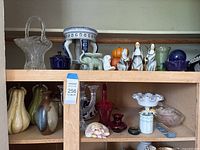 Shelf showing assortment of ceramic and glass decor pieces detailed in lot