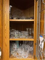 Cabinet shelves showing assorted glasses, tumblers, goblets, shot glasses, serving bowl and platter