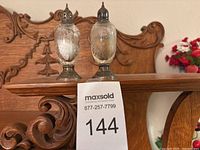 Front view of both etched glass shakers showing sterling caps and bases with MaxSold tag 144