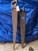 Both large hand saws leaning against tarp backdrop