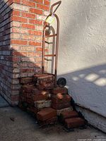 Hand truck leaned against wall atop stacked bricks