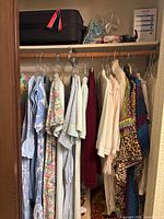 Closet rod with assorted women’s garments, top shelf with suitcase and hair curlers