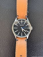 Front view of watch showing dial, hands, indices, day-date window, and leather strap