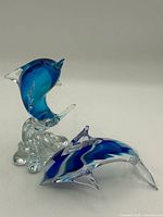 Both glass dolphin figures: one on clear wave base, one free-standing