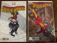 Front view of both Spider-Woman Issue 001 comic books showing distinct cover art in protective sleeves.