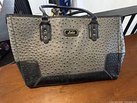 Front view of grey ostrich-embossed Lula tote purse with black trim and handles
