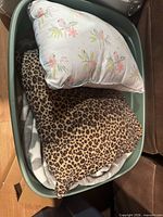 Bin showing floral print throw pillow, leopard print hooded blanket, additional blanket
