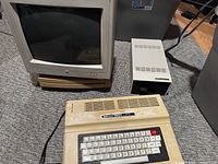 Radio Shack TRS-80 Color Computer 2, Apple monitor, Apple LC II and Tandy drive housing grouped on floor