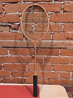 Full racquet front view against brick wall showing overall wear and missing strings
