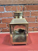 Front view showing brass lantern, glass panels, hinged door, feet, vented top, handle