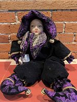 Full view of jester doll seated showing costume, bells, and overall condition