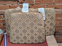 Front view of three patterned cushions against brick wall showing design and overall condition