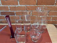 Six assorted glass vases on table against brick wall