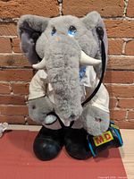 Full view of plush elephant doctor standing against brick wall