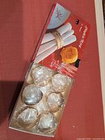 Closed box with six plastic-wrapped brass napkin rings visible