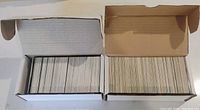 Two open white cardboard boxes filled with rows of trading cards viewed from top