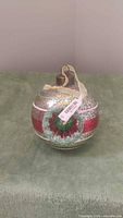 Front view of crackled silver-gold glass ball ornament with red band, glittered wreath, and gold ribbon hanger