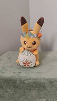 Front view of Pikachu plush showing facial features, floral crown and cushion