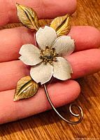 Brooch on hand showing scale, silver petals, gold leaves, curved stem