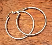 Both sterling silver hoop earrings on wood surface, showing full shape and clasps