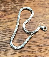 Full view of sterling silver box link bracelet laid in curve