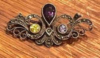 Front view of brooch showing pear amethyst, yellow and lilac stones, and marcasite scrollwork