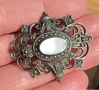 Front view of sterling silver filigree brooch with marcasite and mother of pearl center